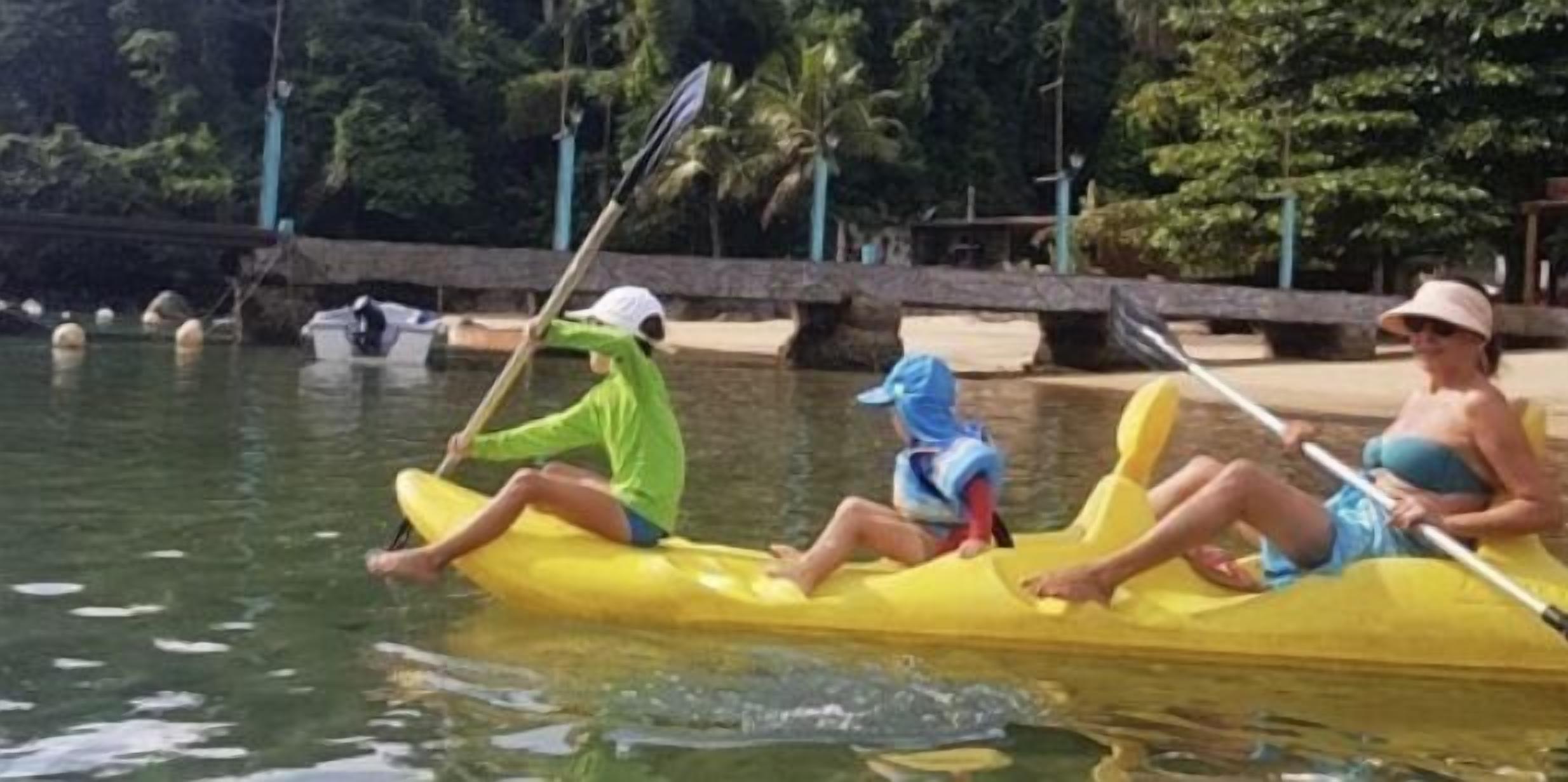 Two people in a yellow kayak on a calm body of water, surrounded by greenery.