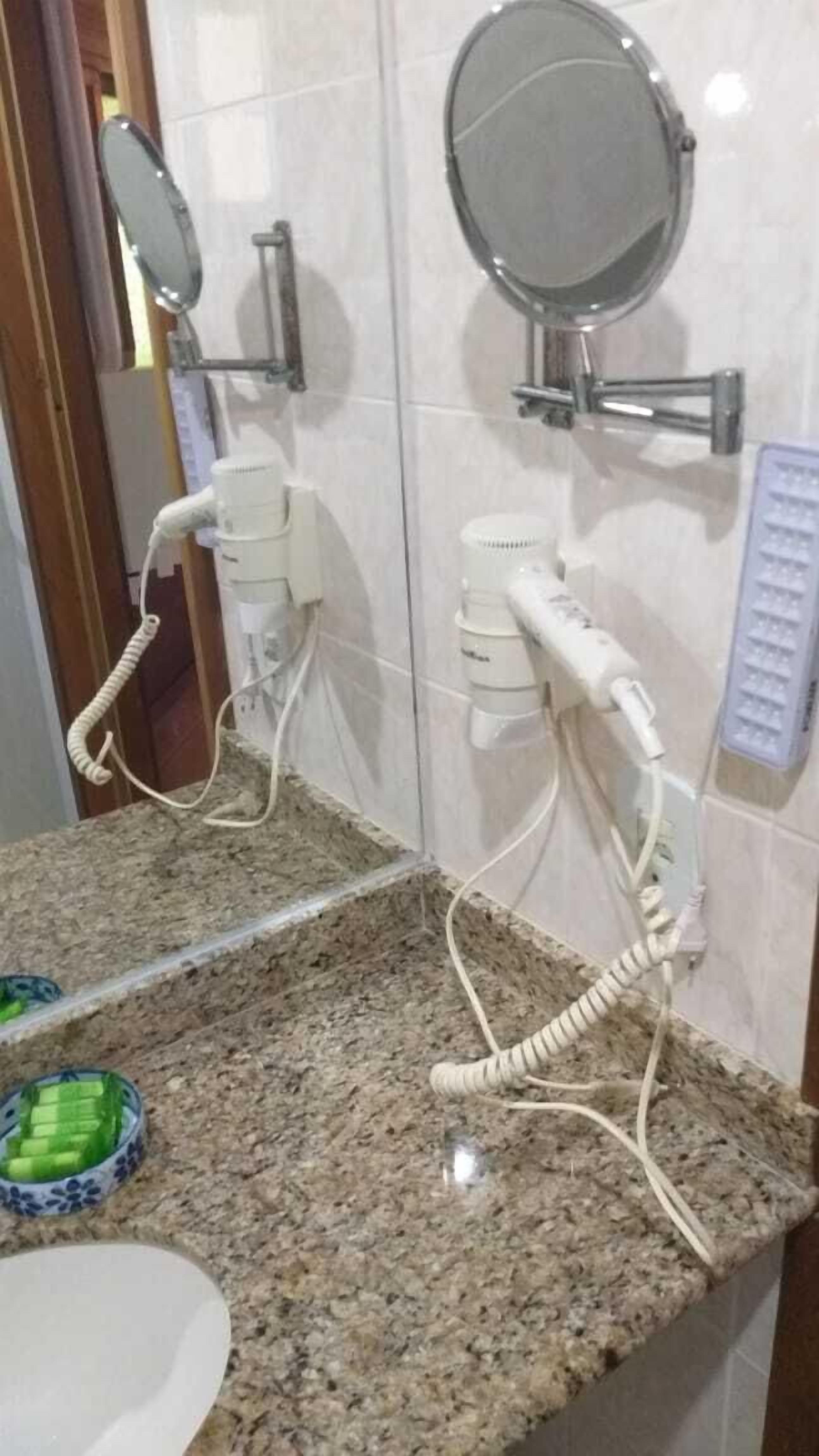 A bathroom with two hair dryers mounted on the wall, a mirror, and a sink with a granite countertop.