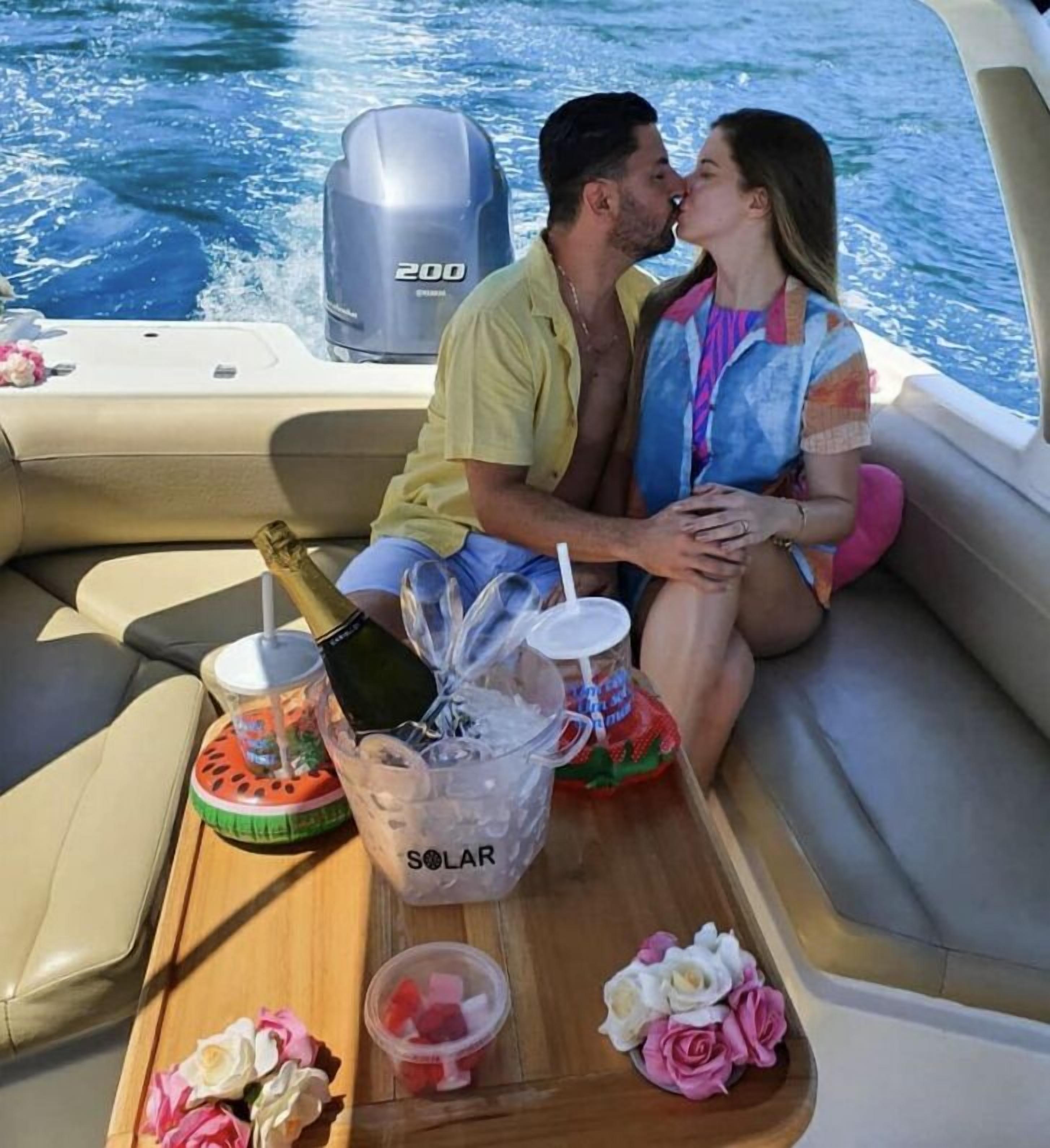 A couple on a boat with a speedboat engine, a bottle of champagne, and a drink cooler labeled "SOLAR" on the deck.