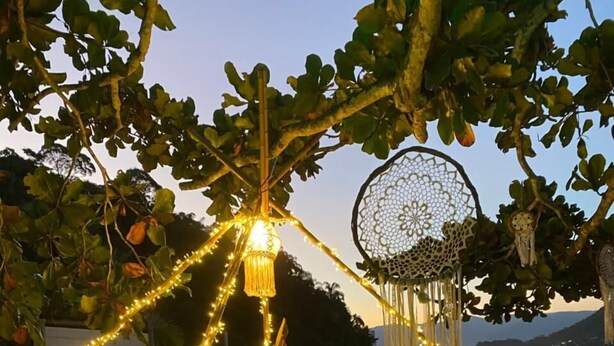 Escena de playa con luces colgantes, un brasero y atrapasueños decorativos.