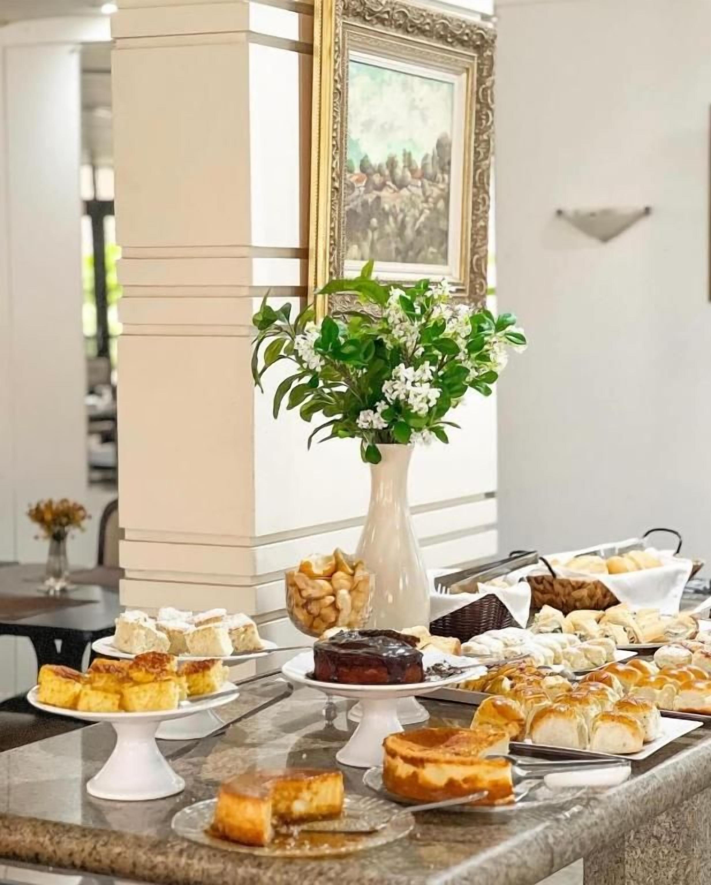 Uma mesa de buffet com diversos doces e sobremesas, um vaso de flores e um quadro na parede.