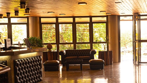 Un hall d’entrée avec un plafond en bois, un comptoir d’accueil, un canapé et de grandes fenêtres donnant sur un paysage verdoyant.