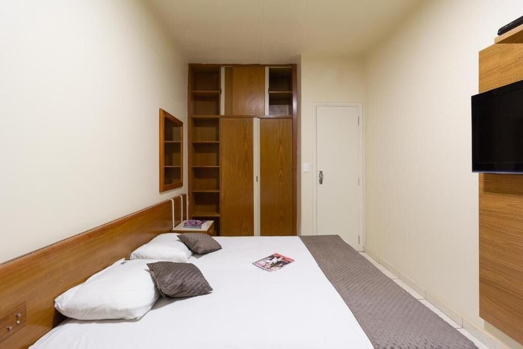 A hotel room with a bed, a TV, a wardrobe, and a small shelf.