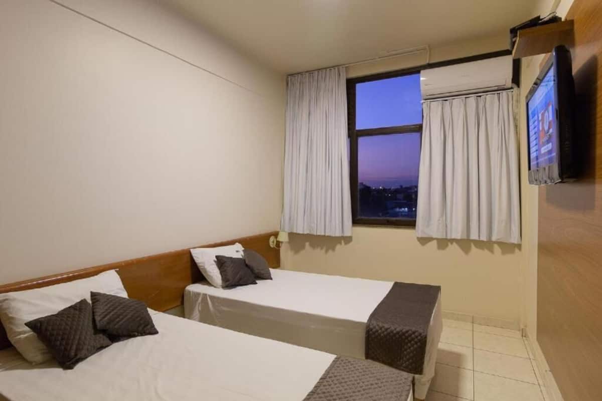 A hotel room with two beds, a TV, and a window with curtains.