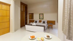 Une chambre d’hôtel avec un lit, une table de chevet, une armoire en bois et une table à manger avec des assiettes de nourriture.