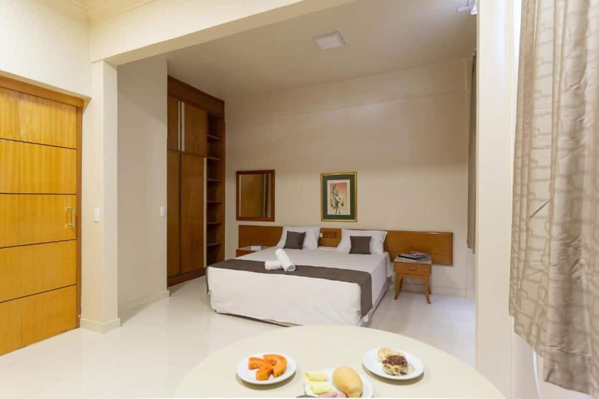 A hotel room with a bed, a nightstand, a wooden wardrobe, and a dining table with plates of food.