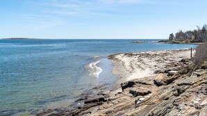 A rocky shoreline with clear water, a distant island, and a house with a dock.