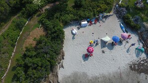 Ein Luftbild eines Strandes mit mehreren Sonnenschirmen, Liegestühlen und einem Zelt.