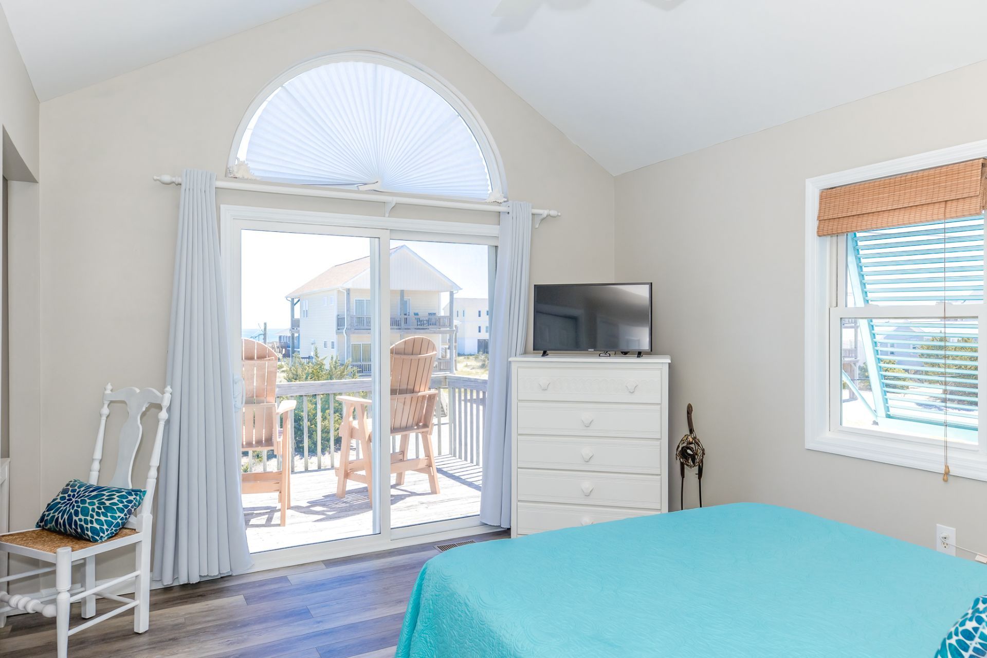 A bedroom with a bed, a dresser, a TV, and a balcony with chairs.