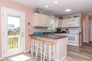 A kitchen with a central island, bar stools, a microwave, and a stove.