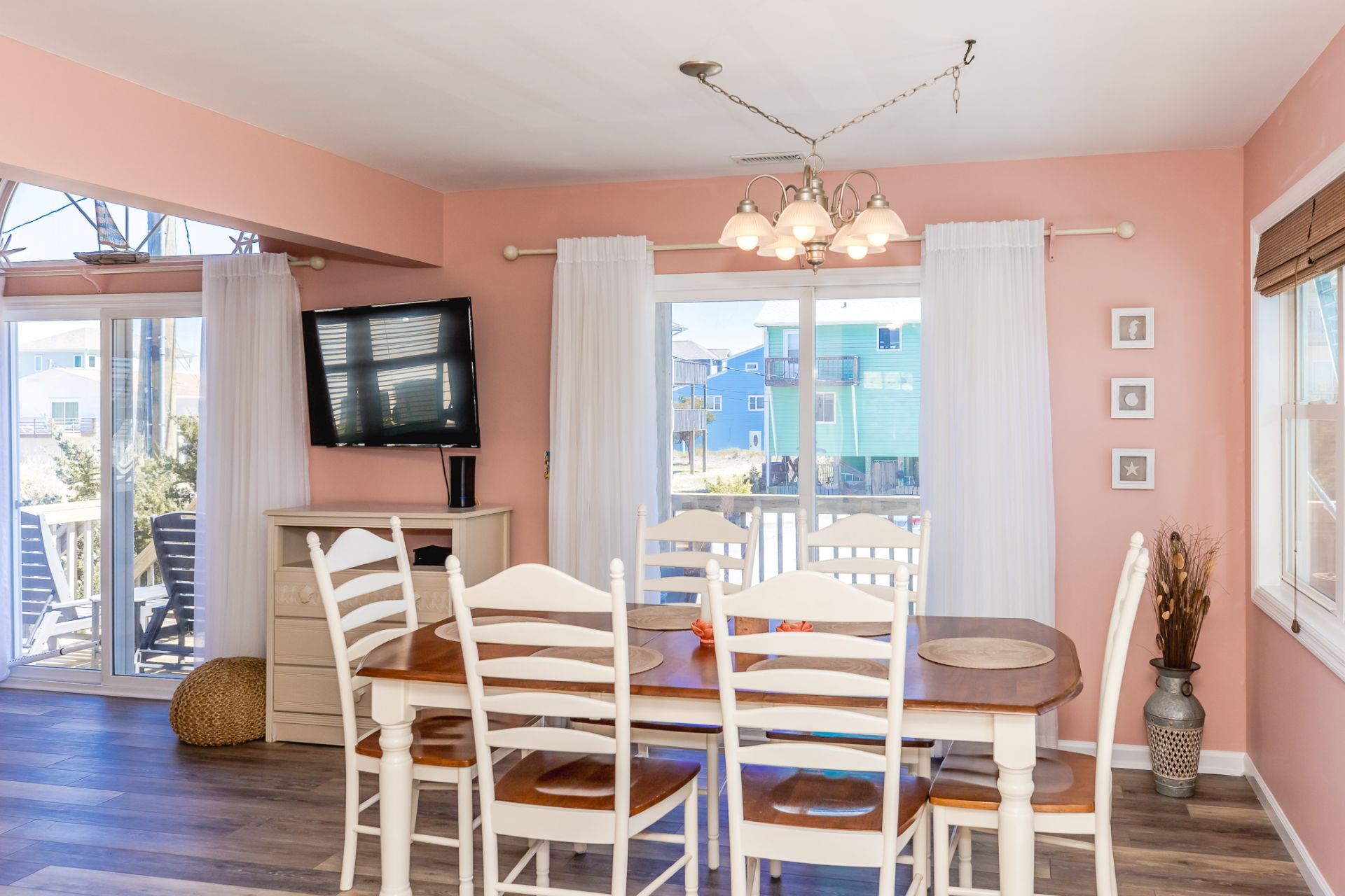 A dining area with a table and chairs, a television on the wall, and a view of buildings outside.
