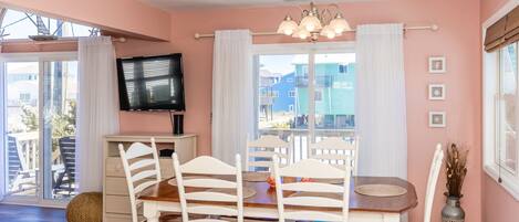 A dining area with a table and chairs, a television on the wall, and a view of buildings outside.