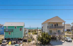 Uma área residencial costeira com casas de dois andares, uma com garagem visível e veículos estacionados, e outra com varanda.