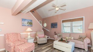 A cozy living room with a sloped ceiling, a ceiling fan, a staircase, and a large window with blinds. - Sea K's - 3 bedroom, 2 bath home in Topsail Beach!  Dog Friendly! (Topsail Beach)