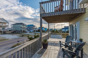Une terrasse en bois avec un banc et des chaises, un pot de fleurs et une vue sur la rue et les maisons voisines.