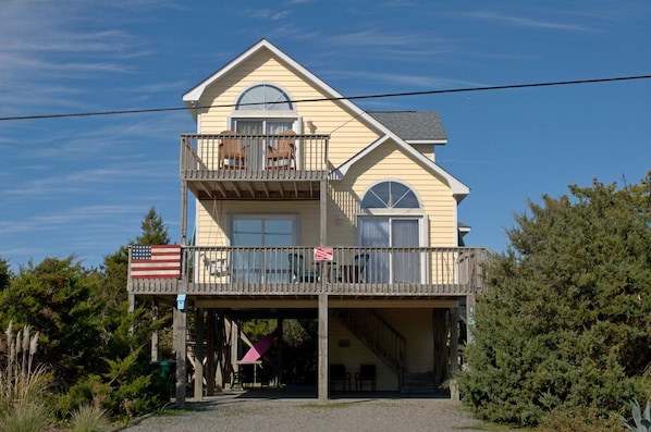 Un immeuble de deux étages doté d’un balcon, d’un drapeau et d’une enseigne indiquant qu’il propose des locations de vacances.