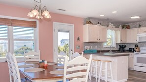 A kitchen with white cabinets, a wooden island with stools, and a view of the outside through the window. - Sea K's - 3 bedroom, 2 bath home in Topsail Beach!  Dog Friendly! (Topsail Beach)