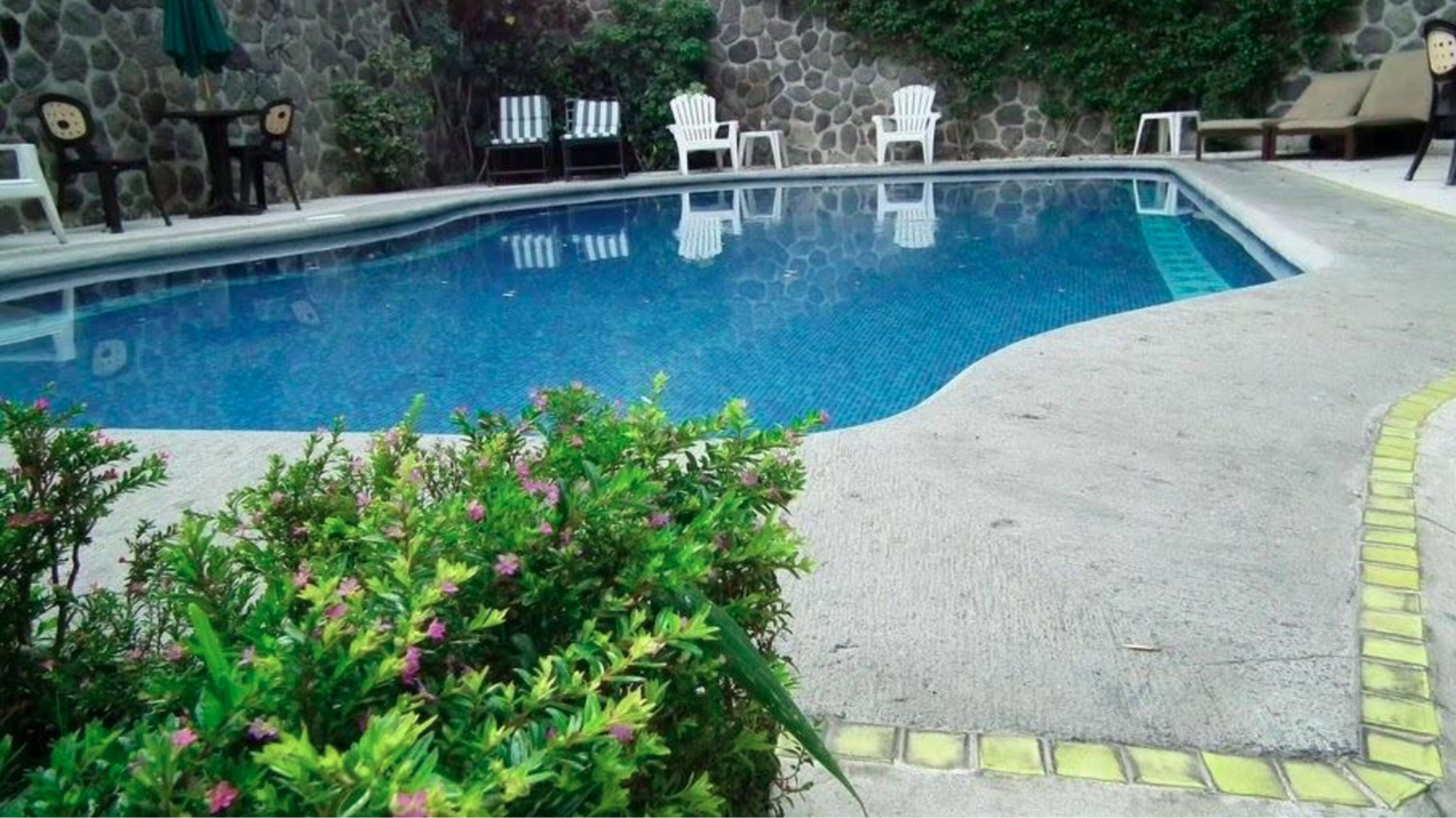 Una piscina con muretto in pietra sullo sfondo, circondata da sedie a sdraio e un tavolino.