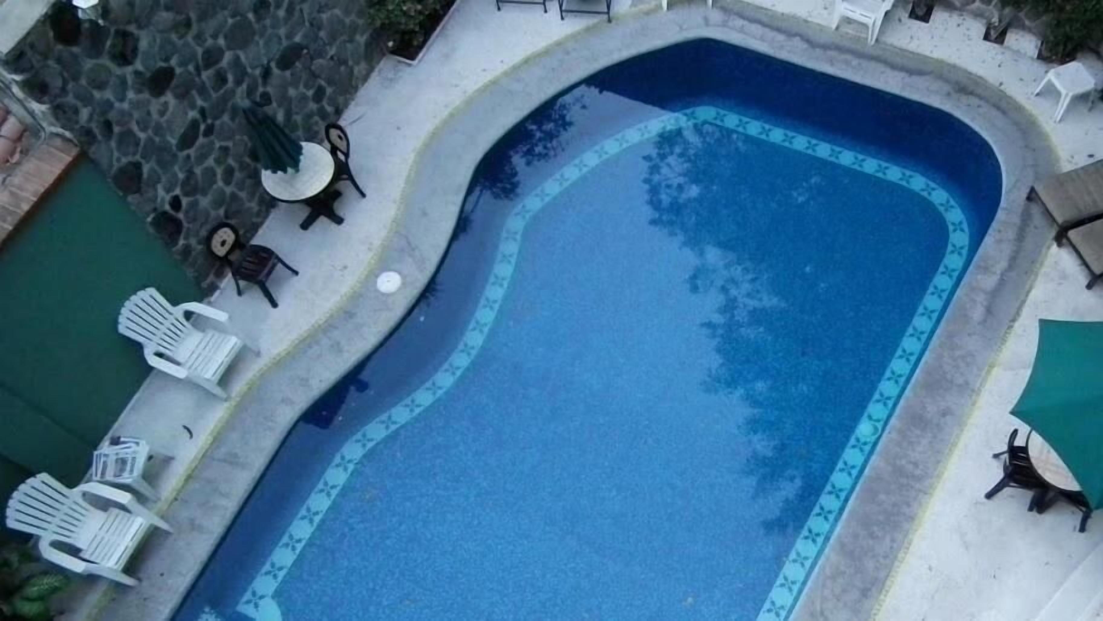 Ein Pool mit geschwungener Kante, umgeben von Liegestühlen und einer Steinmauer.