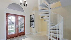 A spacious foyer with a wooden door, a white spiral staircase, and a chandelier. - Waterfront Home With Pool and Foosball Table (Marco Island)