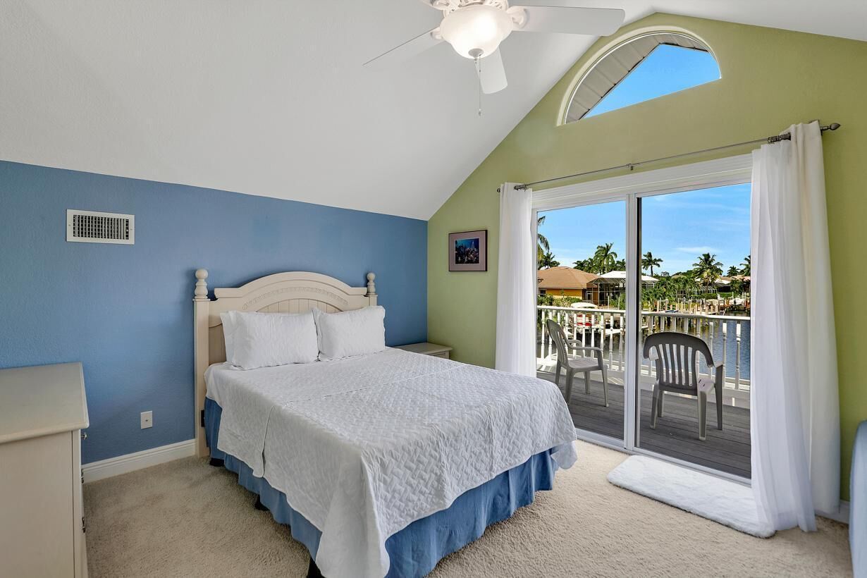 A bedroom with a bed, a ceiling fan, a window, and a view of a marina.