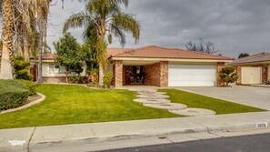 A residential house with a brick facade, a tiled roof, and a front yard with a lawn and palm trees.