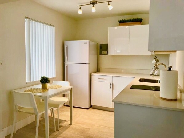 A compact kitchen with white cabinetry, a refrigerator, a sink, and a dining area with a table and chairs. - Oasis at Hollywood - Sleeps 5 - Unit 1 (Hollywood)