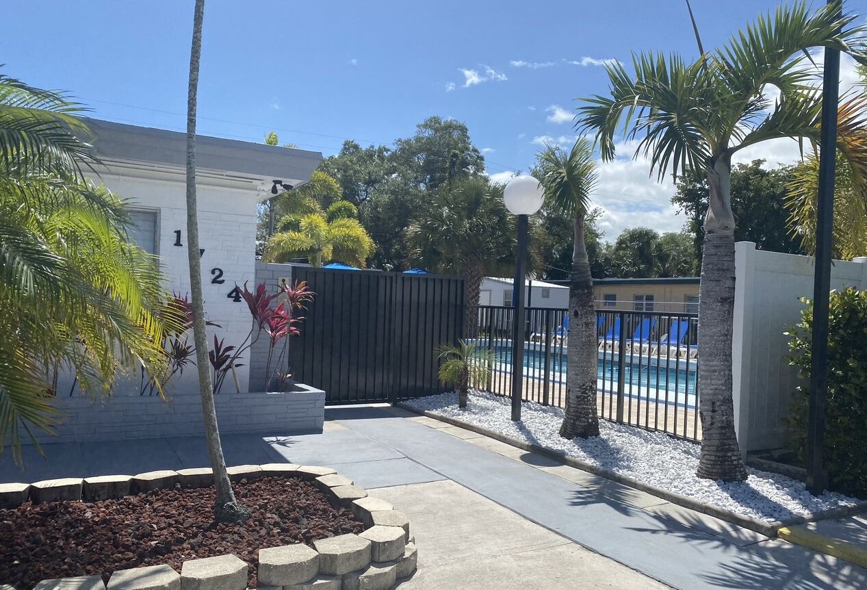 Une propriété résidentielle dotée d’une piscine, de palmiers et d’une entrée sécurisée par un portail.
