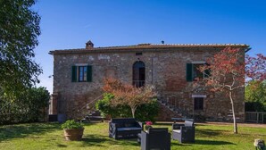 A stone building with a small staircase leading to a door, surrounded by a well-maintained lawn and potted plants. - Villa La Pievina (Asciano)