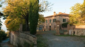 A stone building with a gravel driveway, a tree, and a metal gate. - Villa La Pievina (Asciano)