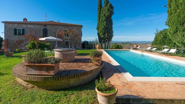 A pool area with a stone building, outdoor seating, and a view of the countryside. - Villa La Pievina (Asciano)