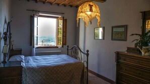 A bedroom with a bed, a window with an open shutter, a radiator, a wooden dresser, and a hanging light fixture. - Villa La Pievina (Asciano)