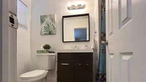 Un baño con inodoro, un armario de madera oscura, un lavabo con espejo arriba y una cortina de ducha.