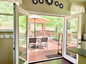 An open sliding glass door leading to an outdoor patio with a table and chairs, a wooden deck, and a stone wall.