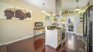 A modern kitchen with a central island, stainless steel appliances, and a dining area with outdoor access. - The Fun House! Hot tub, Espresso Bar, Views, Foosball, Fire Pit, More! (Durango)