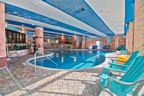 An indoor swimming pool with a stone wall backdrop, lounge chairs, and a tiled floor. - Absolute Beach. Oceanfront. Pet Friendly. (Myrtle Beach)