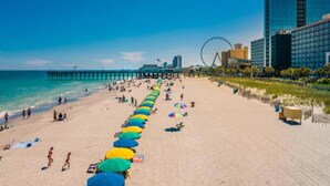 Ein Strand mit einer langen Reihe von Sonnenschirmen, einem Steg und einem Riesenrad im Hintergrund.