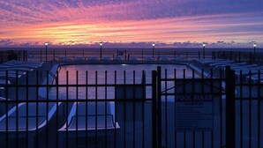A pool area with a sunset view, a fence, and a sign indicating pool rules.
