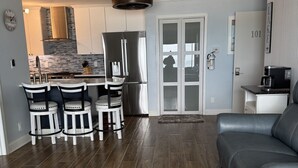 A modern kitchen with a dining area, a gray leather sofa, and a patterned rug.