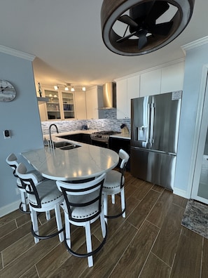 A modern kitchen with a central island, stainless steel appliances, and a clock on the wall.