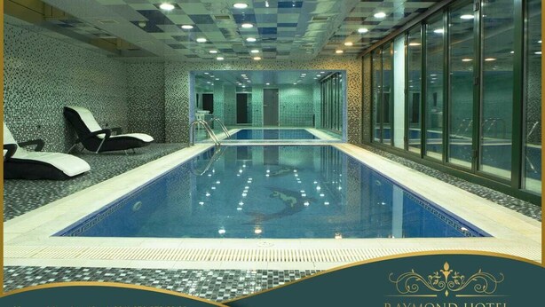 Una piscina interior con baldosas de techo a cuadros, paredes de vidrio y sillones de descanso.