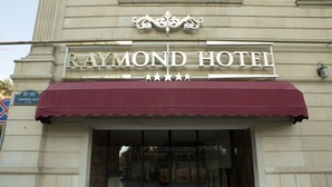 El exterior del Hotel Raymond, con un toldo color granate y un cartel que indica la dirección 87-101.