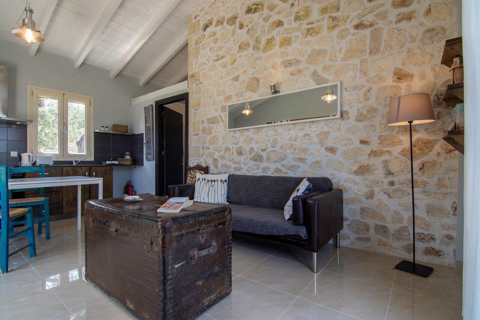 A rustic interior with a stone wall, a sofa, a vintage trunk, and a kitchen area with a window.