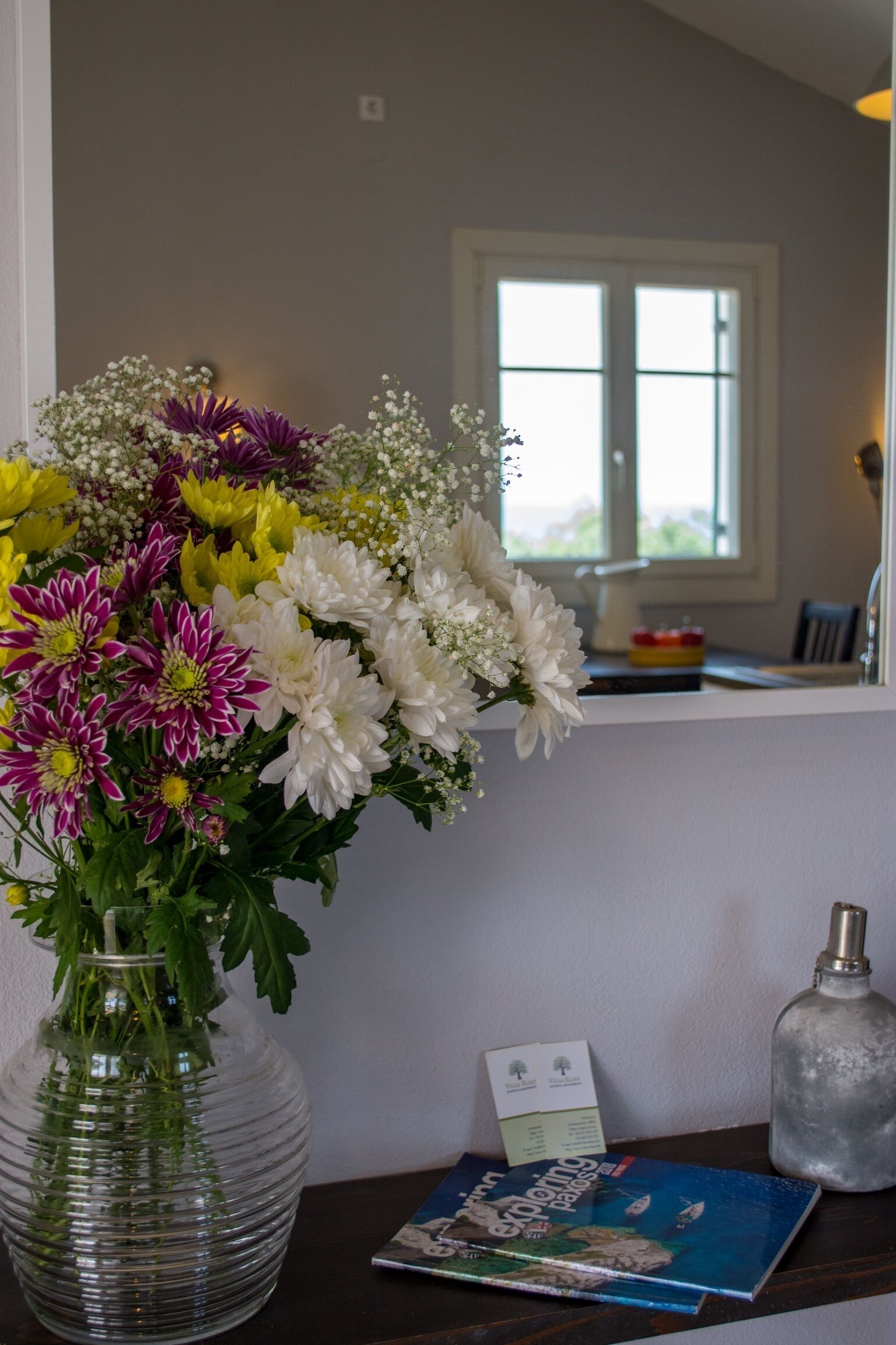 A clear view of a room with a large window, a vase with flowers, a book, and a bottle on a table.