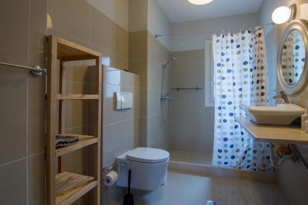 Een badkamer met toilet, douche en wastafel. Er is een houten schap en een douchegordijn met stippen.