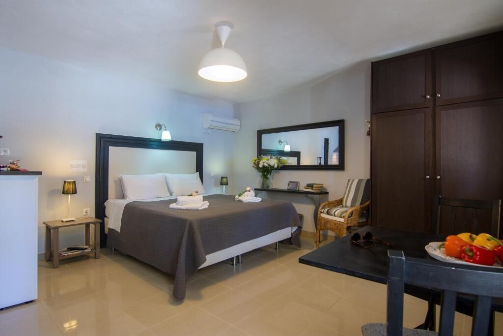 Habitación de hotel con cama, mesita de noche, lámpara, silla y una mesa de comedor con fruta.