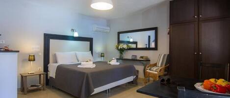 Ein Hotelzimmer mit Bett, Nachttisch, Lampe, Stuhl und einem Esstisch mit Obst.
