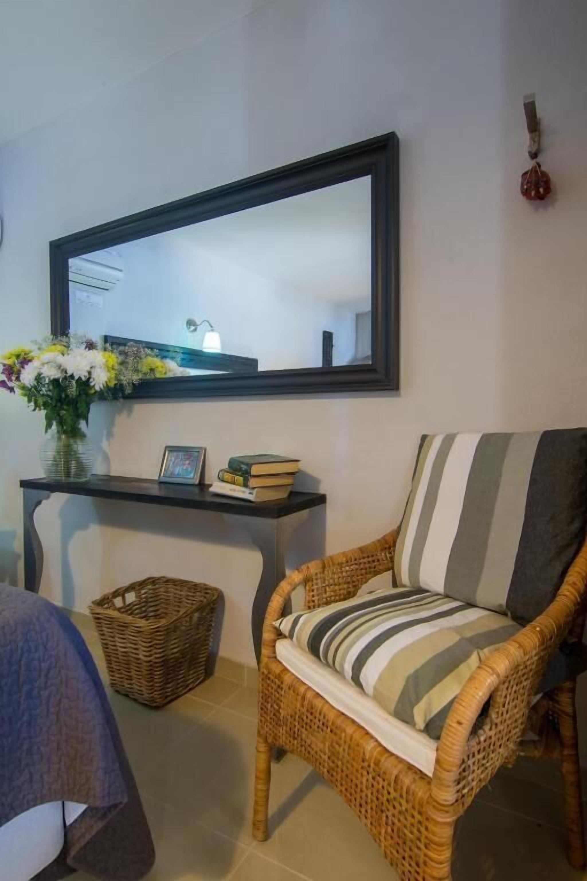 A wicker chair with striped cushions, a small table with a vase of flowers, and a framed mirror on the wall.