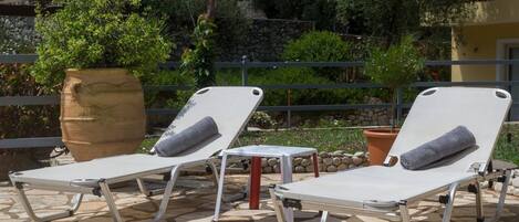 Deux chaises longues avec coussins sur une terrasse en pierre.
