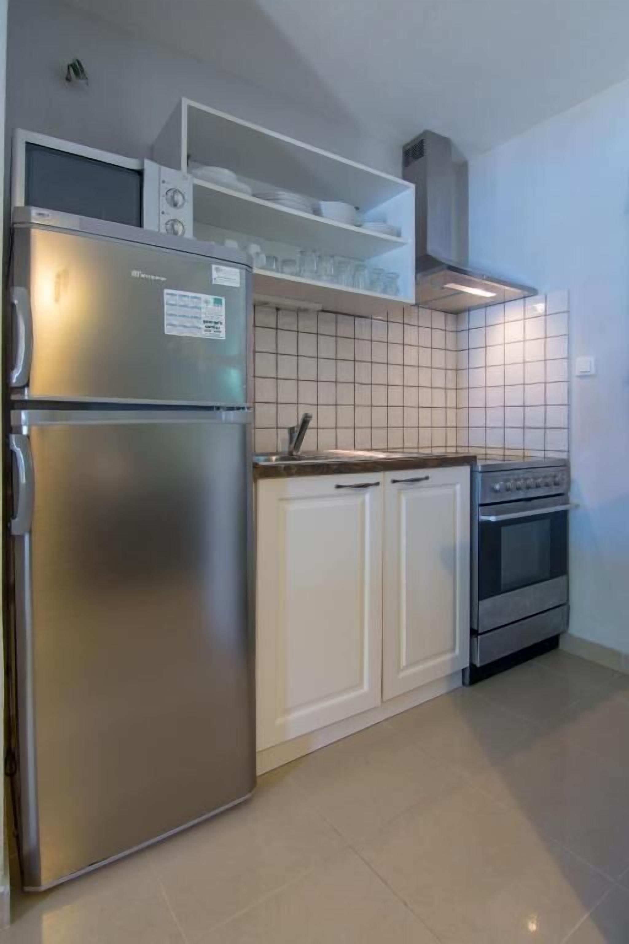 A kitchen with a stainless steel refrigerator, white cabinets, a stove, and a tiled backsplash.